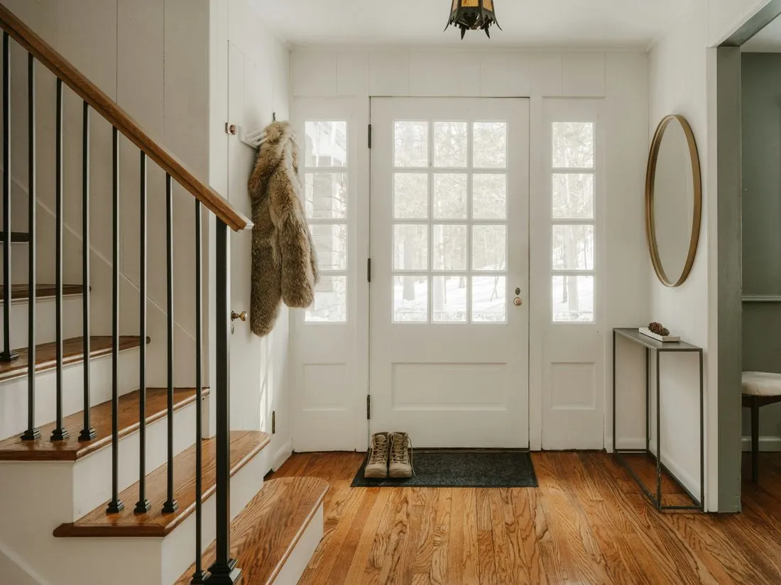 Warm home entryway with a wooden staircase and a glass front door letting in daylight