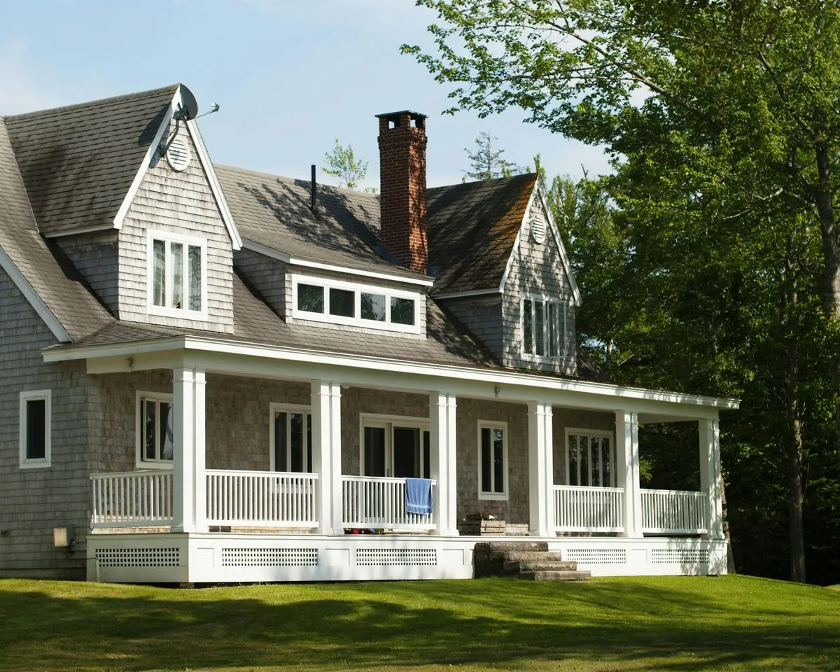 Coastal shingle home with a white porch and clean siding surrounded by trees